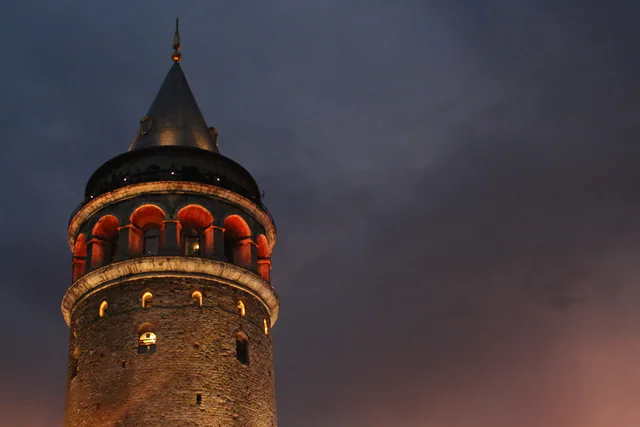 The illuminated upper levels of Galata Tower against the evening sky.